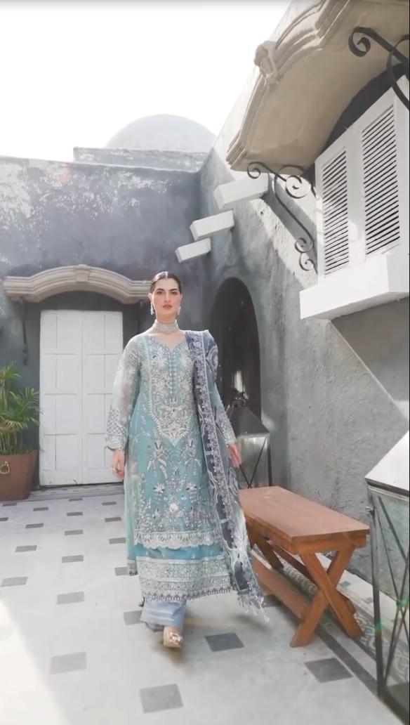 Woman in a light blue and gray traditional outfit standing in an outdoor setting.