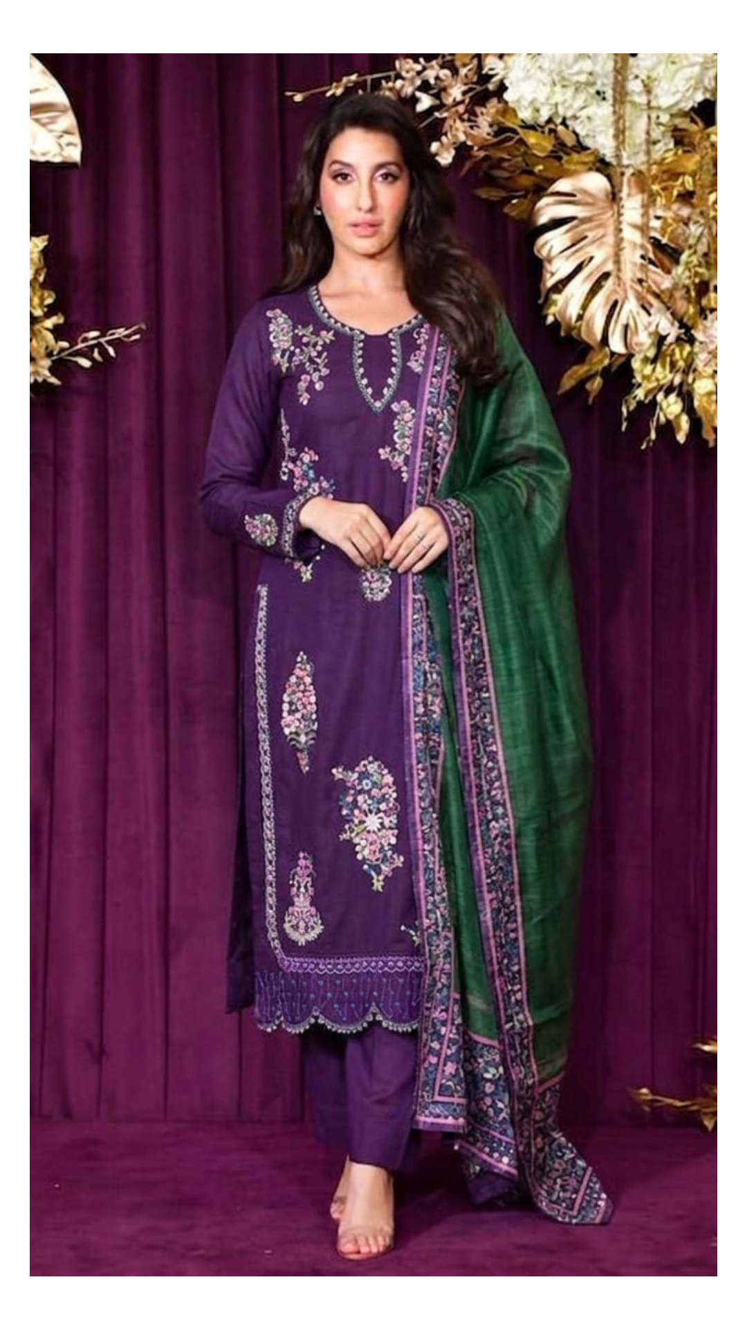 Woman wearing a purple embroidered outfit with a green dupatta against a purple curtain background