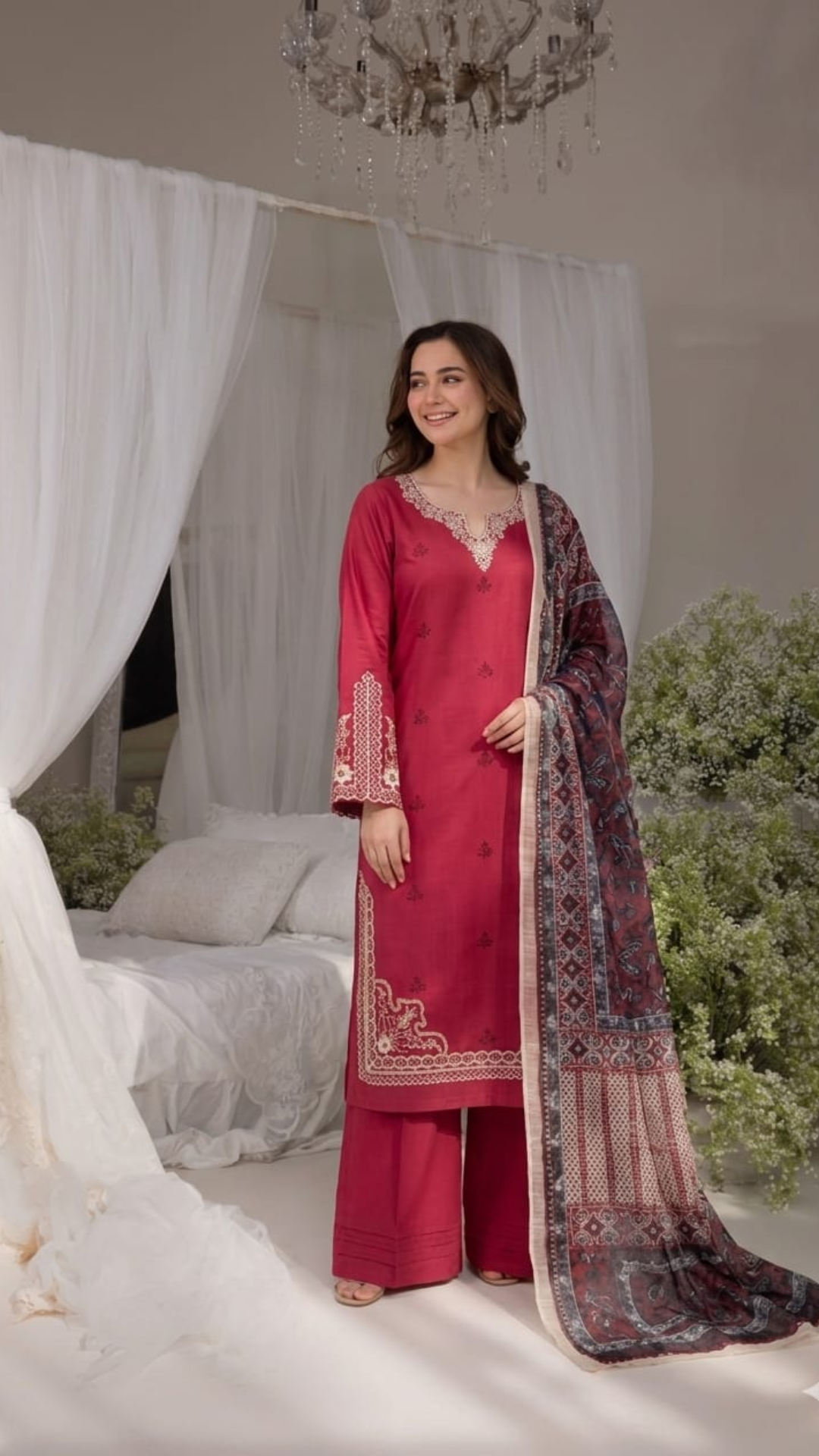 Woman in a pink traditional outfit with a patterned dupatta standing in a decorated room.