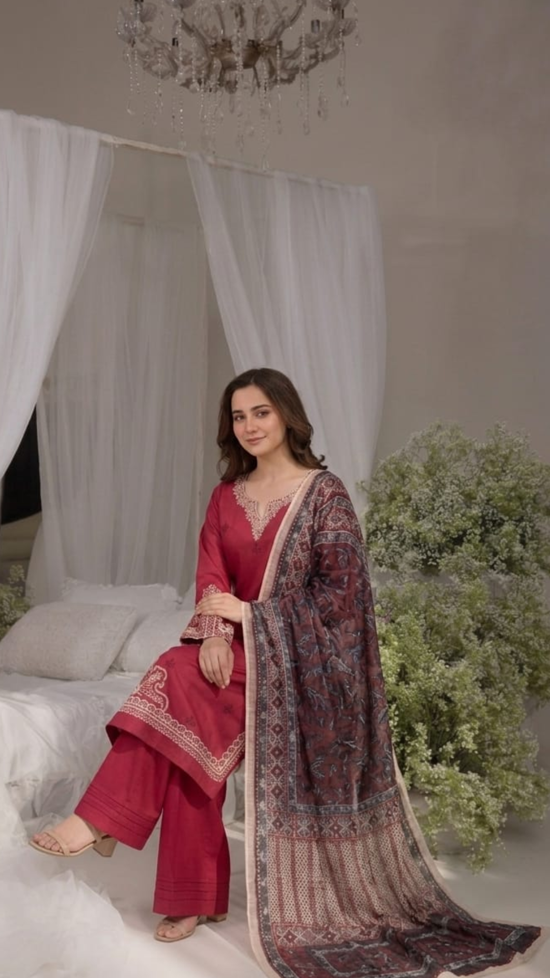 Woman in a red traditional outfit with a patterned dupatta in a decorated room.