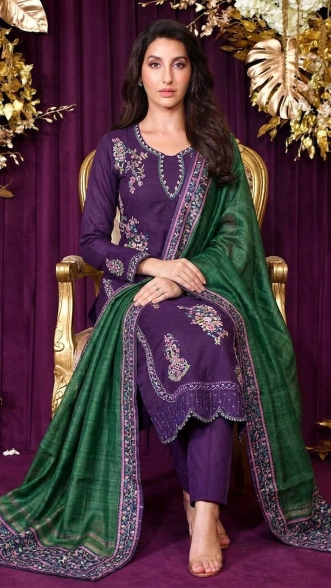 Woman in a traditional outfit with purple and green dress against a purple curtain background
